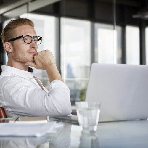 Businessman with laptop on desk in office thinking