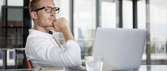 Businessman with laptop on desk in office thinking